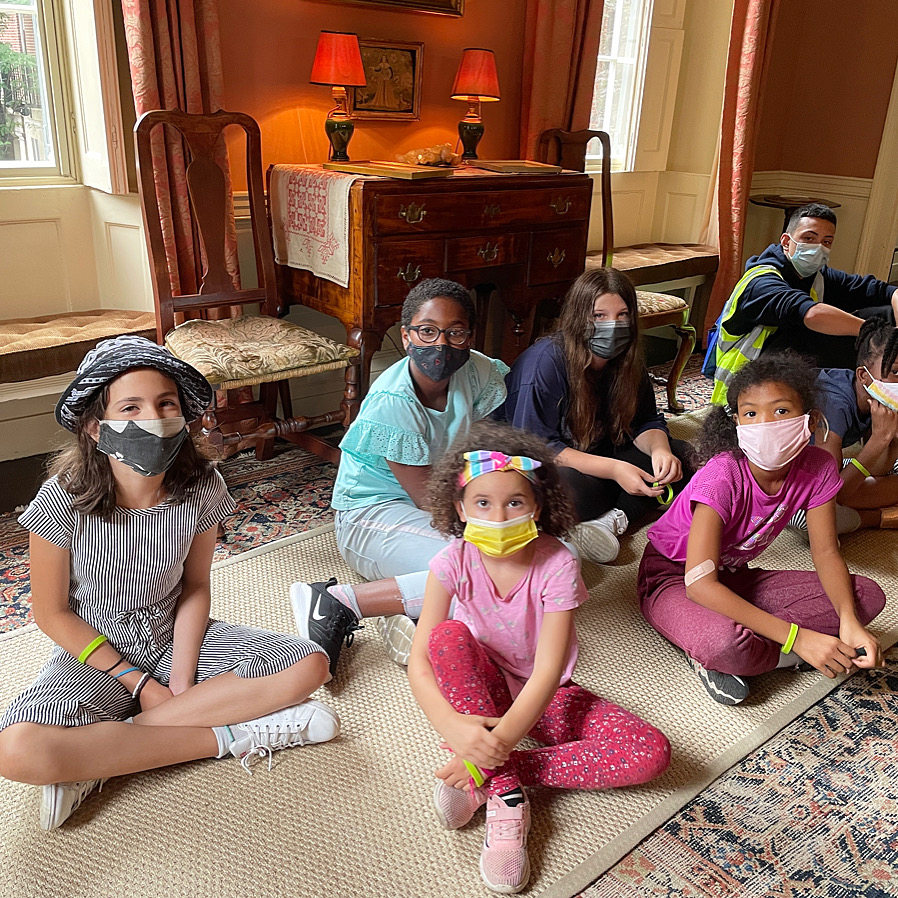 A group of children sitting on the parlor floor and wearing masks