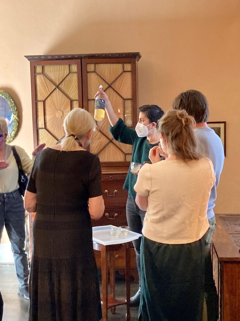 A wine bottle is held up and observed by visitors in a period room.