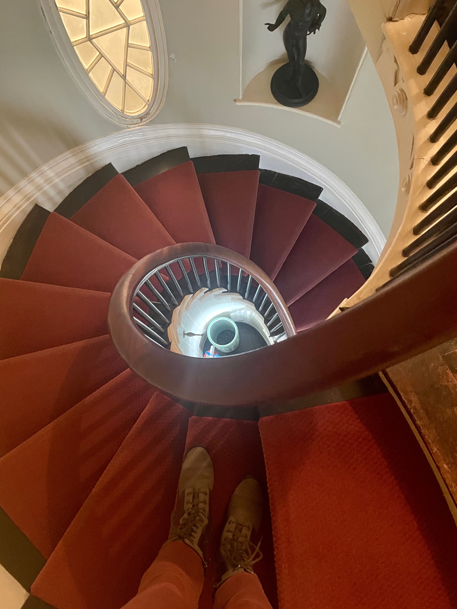 Looking down a spiral staircase with a red carpet. A pair of feet is walking down.